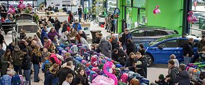 Gro&szlig;er Ausstellungsraum im �koda Autohaus, gef&uuml;llt mit vielen Menschen. In der Mitte sind lange Tische voller bunter Schulranzen. Mehrere �koda-Fahrzeuge stehen zwischen den Besuchern. Rosa Flamingo-Dekorationen h&auml;ngen im Raum.