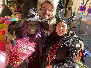 rei verkleidete Personen � eine Hexe mit gr&uuml;nem Gesicht und spitzem Hut, eine Person im wei&szlig;en B&auml;renkost&uuml;m und eine als Maleficent verkleidete Frau � posieren lachend, bunte Luftballons im Hintergrund.