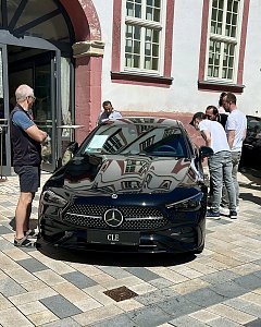 Schwarzer Mercedes CLE steht vor einem historischen Geb&auml;ude in Heiligenstadt. Mehrere M&auml;nner begutachten den Wagen, das Auto spiegelt die Fensterfront des Geb&auml;udes.