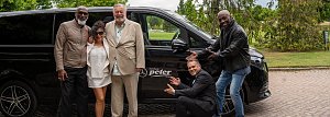 Gruppenfoto vor Shuttlebus: Fünf Personen, darunter vier Männer und eine Frau, posieren lachend vor einem schwarzen Mercedes-Benz Shuttlebus mit dem Logo „Autohaus Peter“.