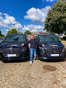 Daniel Kemp, Vorsitzender der Mukoviszidose Selbsthilfe e.V., steht mit ausgebreiteten Armen zwischen zwei schwarzen Mercedes-Benz Transportern mit Autohaus Peter-Logo.