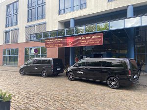 Shuttlebusse vor Hotel: Zwei schwarze Mercedes-Benz Shuttlebusse mit Autohaus Peter-Logo stehen vor dem Radisson Blu F&uuml;rst Leopold Hotel in Dessau, vor einem Banner zur Veranstaltung Music meets Dinner.