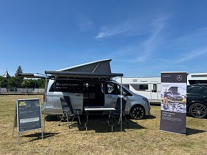 Ein silberner Mercedes-Benz Campingbus mit ge&ouml;ffnetem Aufstelldach und Markise steht auf einer Wiese beim Leichtathletik-Meeting Anhalt 2025. Vor dem Fahrzeug stehen ein Tisch mit St&uuml;hlen, ein Aufsteller und ein Werbebanner, im Hintergrund sind weitere Camper und Fahrzeuge zu sehen.