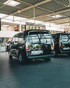 Ein schwarzer Opel-Transporter steht in einem hellen Autohaus mit gro&szlig;en Glasfenstern. 