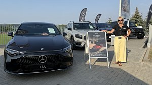 Eine Frau mit schwarzem Polohemd, gelber Hose und Sonnenbrille steht neben einem Aufsteller mit Werbung f&uuml;r den neuen Mercedes CLA. Links im Bild ein schwarzer Mercedes CLA, daneben weitere Mercedes-Modelle in Wei&szlig; und Schwarz. Im Hintergrund wehen schwarze Fahnen mit Mercedes-Logo. Aufnahme beim Leichtathletikmeeting in Sondershausen.