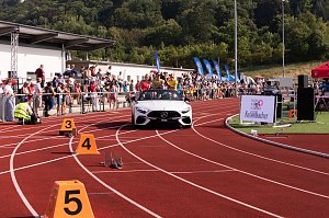 Wei&szlig;es Mercedes-Cabrio f&auml;hrt auf die rote Tartanbahn des Stadions ein. Auf dem R&uuml;cksitz sitzen mehrere Sportlerinnen, w&auml;hrend Zuschauer am Rand applaudieren.