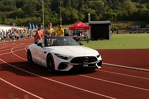 Nahaufnahme des wei&szlig;en Mercedes-Cabrios auf der Laufbahn. Drei Sportstars sitzen auf der R&uuml;ckbank, jubeln und winken dem Publikum zu.