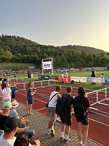 Zuschauer blicken von der Trib&uuml;ne auf die Laufbahn. Eine gro&szlig;e LED-Leinwand zeigt das Logo des Autohauses Peter. Im Hintergrund Waldh&uuml;gel bei Sonnenuntergang.