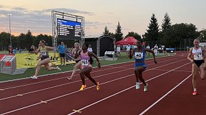 Sprint-Finale &uuml;ber 100 Meter der Frauen. Mehrere Athletinnen im Endspurt kurz vor der Ziellinie, im Hintergrund eine Anzeigetafel mit Namen und Zeiten. Zuschauer und Kampfrichter beobachten den Zieleinlauf