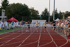 Mehrere Athleten im H&uuml;rdenlauf springen gleichzeitig &uuml;ber die H&uuml;rden. Zuschauer verfolgen den Lauf von der Trib&uuml;ne und am Bahnrand.