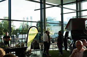Ein Messestand mit gelb-gr&uuml;nem Banner M&ouml;bius � Gr&uuml;n macht gl&uuml;cklich!. Daneben ein schwarzer Mercedes-Camper mit hochgeklapptem Dach. Zwei M&auml;nner und weitere Personen unterhalten sich.