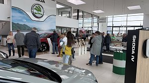 Besucherinnen und Besucher im Autohaus Autowelt Peter w&auml;hrend der Jubil&auml;umsfeier zu 130 Jahren �koda. Im Ausstellungsraum stehen Fahrzeuge, Kranzdekorationen und ein Tisch mit Sektgl&auml;sern.