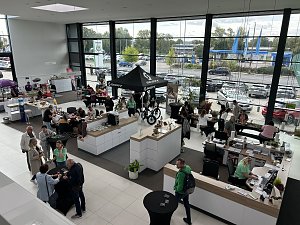 Blick von oben in den hellen Ausstellungsraum des Autohauses Autowelt Peter w&auml;hrend der Feier zu 130 Jahren �koda. Besucherinnen und Besucher sitzen an Tischen, basteln und stricken, andere informieren sich an St&auml;nden, darunter ein SCOTT-Zelt mit Fahrr&auml;dern.