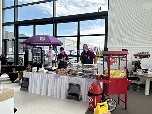 Verkaufsstand mit Snacks und S&uuml;&szlig;waren im Autohaus Autowelt Peter. Unter einem lila Sonnenschirm stehen Verk&auml;ufer, daneben eine rote Popcornmaschine.