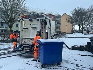 Müllabfuhr leert eine blaue Mülltonne auf einer verschneiten Wohnstraße.