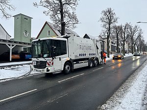 Modernes Müllfahrzeug Garbage Truck of the Future fährt auf winterlicher Straße durch eine Ortschaft.