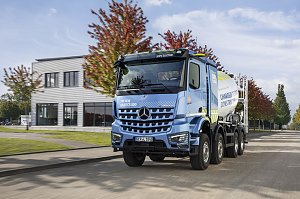 Elektrischer Betonmischer Mercedes-Benz eArocs 400 fährt auf einer Straße vor einem modernen Gebäude