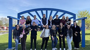 Gruppenfoto: Große blaue XXL-Bank, darauf sitzen mehrere Personen, einige stehen davor und lächeln in die Kamera.