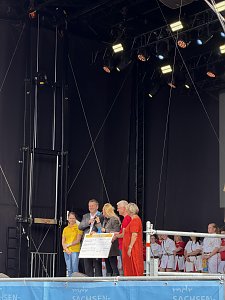Sven Schulze (MP des Landes Sachsen-Anhalt) und Dr. Silvia Ristow (OB Bernburg (Saale)) mit zwei weiteren Personen und einer Moderatorin auf der Bühne während einer Scheckübergabe.