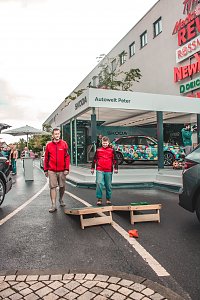 Škoda Roadshow Bühne mit einem bunt beklebten Fahrzeug; davor 2 Besucher, die ein Wurfspiel spielen.
