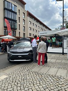 Škoda Roadshow Bühne im Hintergrund; davor graues Skoda Fahrzeug mit mehreren interessierten Personen daneben.