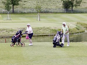 Zwei Golfspieler schieben ihre Trolleys entlang eines Fairways neben einem Wasserhindernis.