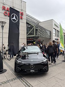 Man sieht einige Teilnehmer und Zuschauer, im Fokus des Bildes steht der CLA Shooting Brake in Schwarz, dahinter eine große schwarze Fahne mit dem weißen Mercedes-Benz Stern.