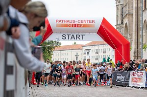Man sieht viele Läufer und Läuferinnen beim Start eines Laufs. Zuschauer fotografieren und im Hintergrund sieht man die Kulisse der Dessauer Innenstadt.