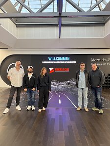 Fünf Personen stehen nebeneinander für ein Gruppenfoto vor einer großen Medienwand. Auf dem Bildschirm hinter ihnen leuchtet der Schriftzug Willkommen zusammen mit dem Logo von Ehrlich Logistics