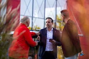 Drei M&auml;nner im Gespr&auml;ch bei der Fahrzeug&uuml;bergabe an den Th&uuml;ringer HC, darunter ein Mann im dunkelblauen Anzug mit Smartphone.