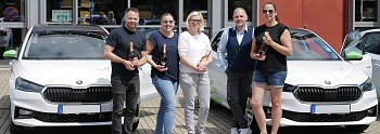 Fünf Personen stehen vor einem modernen Gebäude und posieren mit Champagnerflaschen vor zwei weißen koda-Fahrzeugen. Auf den Autos sind grüne Elemente und das Logo der „Praxisklinik für Zahnheilkunde“ zu sehen. (Autohaus Peter)