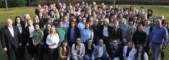 Gro&szlig;es Gruppenfoto im Freien bei der Frauentagsfeier der Autohaus Peter Gruppe. Zahlreiche Frauen und einige M&auml;nner stehen dicht beieinander auf einer Wiese, im Hintergrund kahle B&auml;ume an einem sonnigen Tag.
