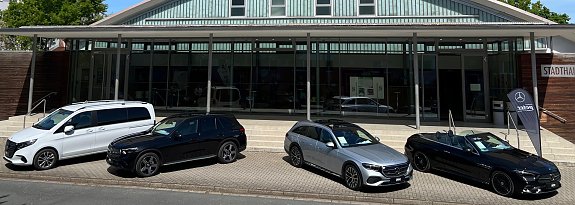 Vor der Stadthalle Wittenberg sind vier Mercedes-Benz-Fahrzeuge in einer Reihe ausgestellt: ein wei&szlig;er Van, ein schwarzer SUV, ein silberner Kombi und ein schwarzes Cabriolet mit offenem Verdeck. Rechts steht eine schwarze Fahne mit dem Logo Autohaus Peter.