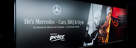 Ein schwarzes Banner mit dem Mercedes-Logo und der Aufschrift He�s Mercedes � Cars, BBQ & Style. Ein Abend f&uuml;r M&auml;nner mit Charakter � und echtem Antrieb. Rechts sind ein Mann mit Weinglas, ein Grillfeuer und der Scheinwerfer eines Mercedes-Autos abgebildet.