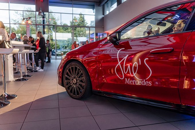 Ein rotes Mercedes-Fahrzeug mit der Aufschrift She’s Mercedes auf der Fahrertür steht in einem hellen Showroom. Im Hintergrund unterhalten sich Menschen an Stehtischen. Mercedes-Benz CLA 250+ mit EQ-Technologie | Energieverbrauch kombiniert: 14,1-12,2 kWh/100 km | CO2Emissionen kombiniert: 0 g/km | CO2-Emissionsklasse: A (Foto: Eric Freytag) Ein rotes Mercedes-Fahrzeug mit der Aufschrift She’s Mercedes auf der Fahrertür steht in einem hellen Showroom. Im Hintergrund unterhalten sich Menschen an Stehtischen. Mercedes-Benz CLA 250+ mit EQ-Technologie | Energieverbrauch kombiniert: 14,1-12,2 kWh/100 km | CO2Emissionen kombiniert: 0 g/km | CO2-Emissionsklasse: A (Foto: Eric Freytag)