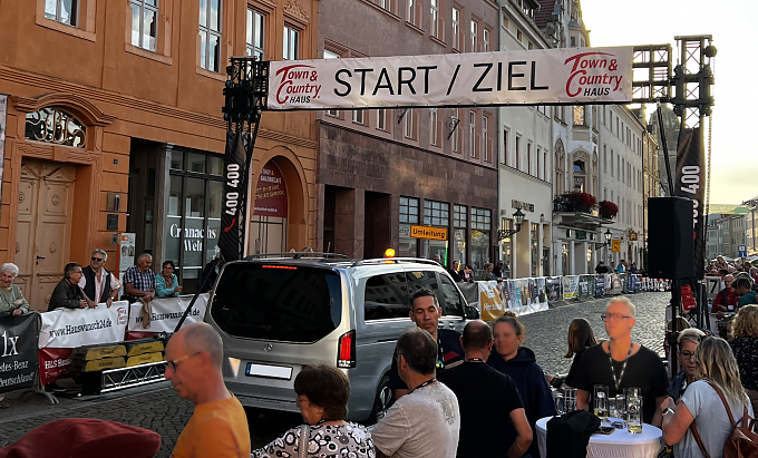 Zu sehen ist die Start Ziel Linie des Radsportrennen in Wittenberg. Darunter befindet sich ein silberner EQV, der als F&uuml;hrungsfahrzeug diente. Rund um die Start Ziel Linie sind hunderte Zuschauer zu sehen.