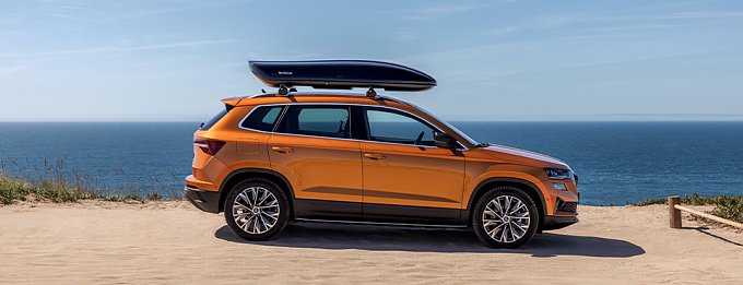 Orangefarbener SUV mit Dachbox an K&uuml;stenstra&szlig;e am Meer geparkt.